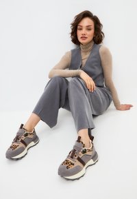 Gilet à rayures grises et pantalon large, associés à des baskets grises avec un accent en imprimé léopard et des éléments en brun foncé.