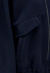 Marineblaues Fleece-Jackett mit Reißverschluss, seitlichen Taschen und gerippten Bündchen am Saum. Weicher Stoff und glatte Oberfläche.