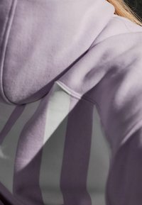 Sudadera morada con un acabado texturizado y un patrón de rayas blancas en contraste a lo largo de la manga, que muestra un diseño moderno y de corte relajado.