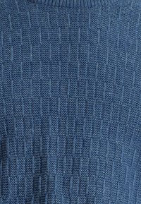 Niebieski sweter dziany o fakturze z pionowymi prążkami. Bluzka wykończona prążkowanym dekoltem i gładkim wykończeniem.