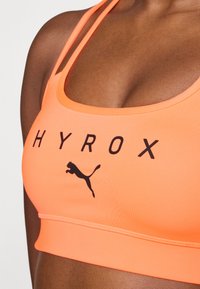 Oransje idretts-BH laget av elastisk stoff, med svart "HYROX"-tekst og Puma-logo. Designet har en scoop hals og smale stropper.