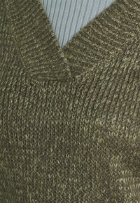 Maglione lavorato a maglia verde oliva con scollo a V, caratterizzato da un motivo testurizzato e diverse spessore del filato, che creano profondità e dimensione.