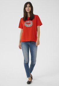 Röd t-shirt av bomull med en design av leopardmönstrade läppar på framsidan. Kombinerad med urtvättade blå skinny jeans och svarta baletttofflor.