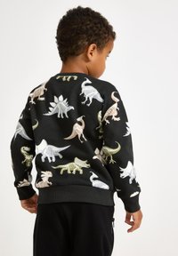 Svart sweatshirt med färgglada dinosaurieskelettmönster. Ribbad mudd och nederkant. Mjuk textur, avslappnad passform. Lämplig för vardagligt bruk.