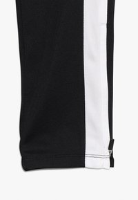 Černé sportovní kalhoty s bílým bočním pruhem, vyrobené z texturovaného materiálu, s rozepínacím otvorem na spodním lemu pro přizpůsobení.