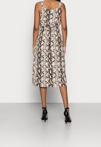 Midiklänning med ormskinnsmönster, breda axelband, figursydd kropp och flödande kjol. Har ett neutralt mönster i beige och svart. Bärs med svarta klackar.