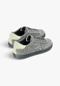 Glittery gray sneakers with a textured finish, featuring a light gray heel, gray laces, and silver skull-and-crossbones logo detail.