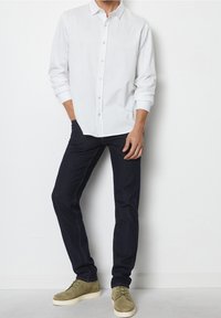 Camicia bianca a maniche lunghe con bottoni beige, abbinata a jeans di denim scuro e scarpe scamosciate verde oliva con suola crema.