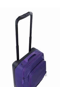 Bolsa morada con ruedas, superficie de tela texturizada, múltiples compartimentos con cremallera y un asa retráctil negra.