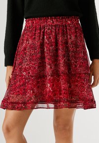 Punainen kuvioitu hame, jossa on kerroksellinen muotoilu ja joustava vyötärö. Kevyt kangas, joka tuntuu ilmavalta, ja siinä on herkkiä kukkakoristeita.