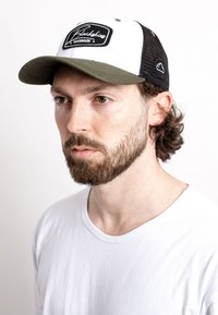 Black trucker cap with white front panel, black mesh sides, and olive green bill. Features "Blackbikes" logo on the front. Worn by a person.