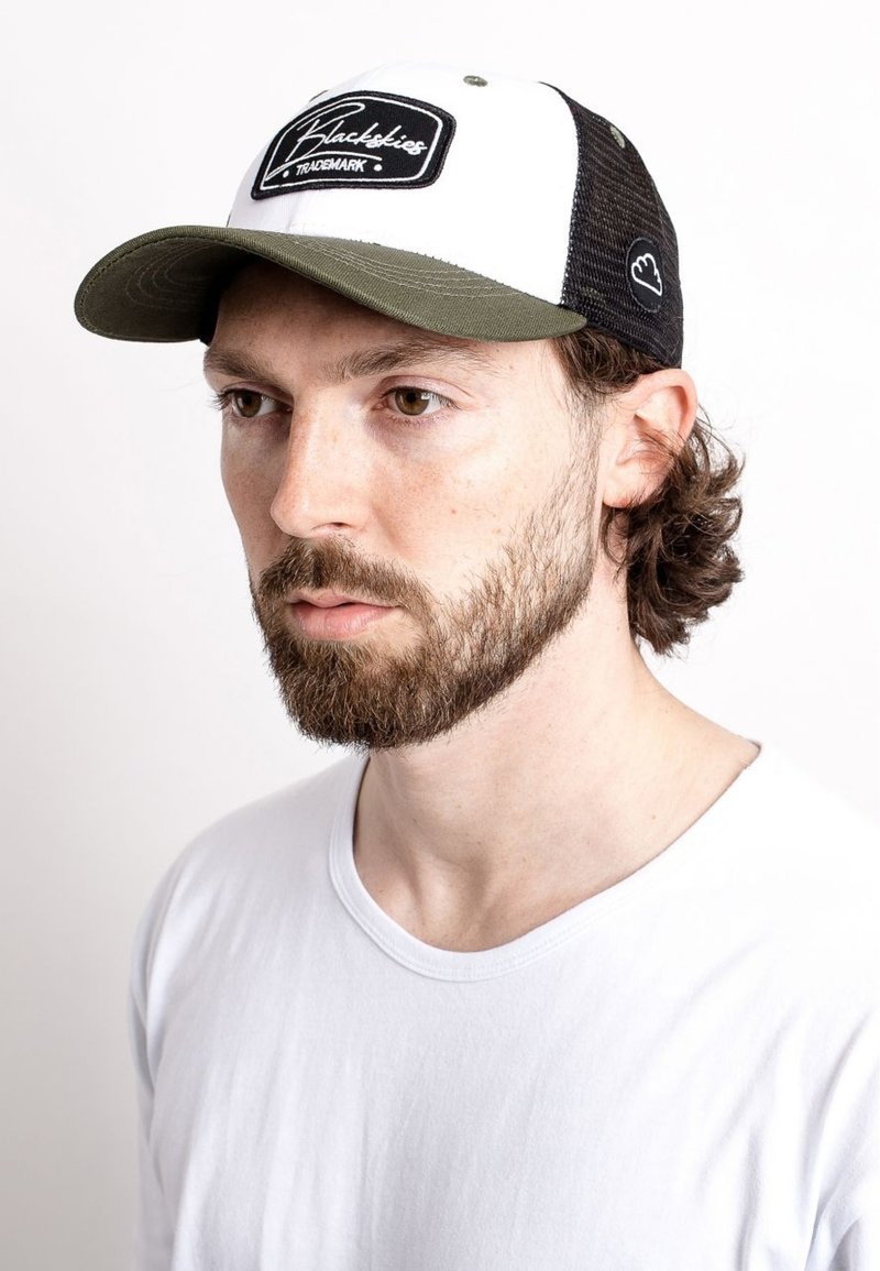 Black trucker cap with white front panel, black mesh sides, and olive green bill. Features "Blackbikes" logo on the front. Worn by a person.