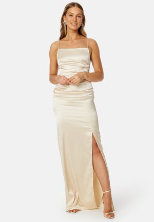 Robe de soirée en satin crème avec un corsage ajusté, des bretelles fines et une fente haute sur la cuisse. Texture lisse avec des détails de drapés subtils.