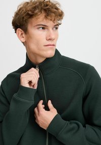 Dark green zip-up sweatshirt with a high collar, ribbed cuffs, and a smooth texture. Features contrasting stitching and metallic zipper.