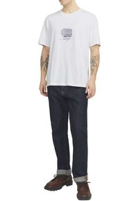 Camiseta de algodón blanca con un estampado gráfico en negro. Combinada con jeans de mezclilla azul oscuro y zapatos marrones con cordones, con dobladillos en los pantalones.