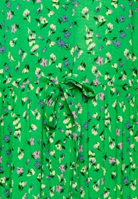 Grön blommig klänning i strukturerad tyg med små lila och vita blommor. Den har en åtsittande liv med midjeband och ett godtyckligt kjol.