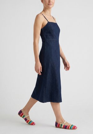 Kvinde i navy denim midi kjole med tynde stropper, gående, iført farverige stribede flade sko med rem.