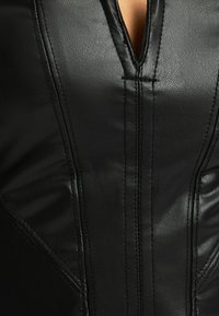 Svart läderplagg med djup V-ringning, sydda detaljer och en jämn yta med diskret glans. Skräddarsydd passform med konturer.