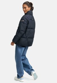 Marineblå puffjakke med høj krave, quiltet mønster og logo-accent på skulderen. Sæt sammen med blå bredbenede jeans og sneakers.