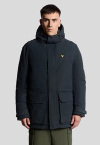 Mörkblå vadderad jacka med hög krage, två framfickor och en liten gul logotyp på övre vänster sida. Slät material, skräddarsydd passform.
