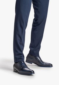 Scarpe da uomo in pelle blu navy con texture liscia, punta rotonda, lacci blu e un design sottile sulla tomaia; abbinate a pantaloni navy su misura.