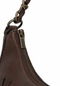 Primo piano di un angolo di borsa in pelle marrone con zip metallica visibile e link della tracolla in catena.