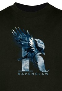 Musta t-paita, jossa on sininen ja valkoinen grafiikka jalopeurasta, jonka siivet ovat levitettyinä. Graafikka toimii päällekkäin tyylitellyn "R":n ja sanan "RAVENCLAW" kanssa.