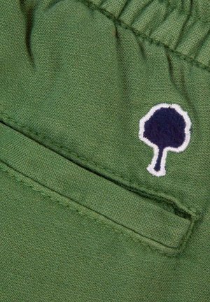 Tissu vert avec couture élastique et un petit arbre bleu foncé brodé avec un contour blanc près de la couture d'une poche.