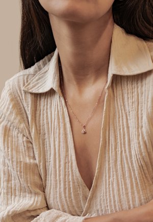 Close-up of woman wearing a beige textured shirt and a delicate gold necklace with a small triangular pendant.
