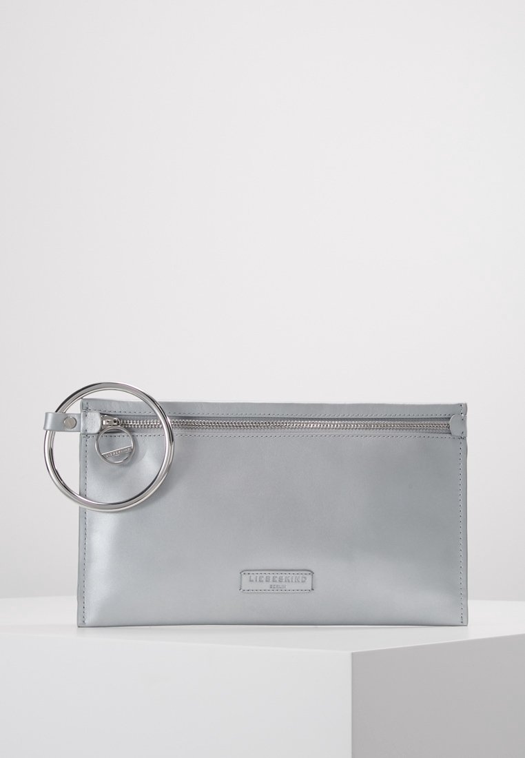 Grå läderclutch med en slät yta, utrustad med ett topsdragkedja och en stor metallring som accent på sidan.