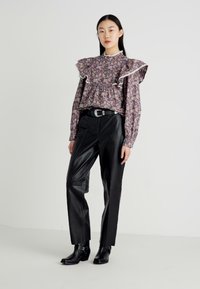 Bluse med blomsterdesign og rynkede skuldre, kombinert med svarte lærbukser og ankelstøvler. Finessene inkluderer en tettsittende midje og belte.