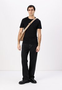 Camiseta negra de manga corta combinada con jeans negros. Un bolso cruzado color marrón claro está colgado de un hombro. El calzado es negro y de suela gruesa.