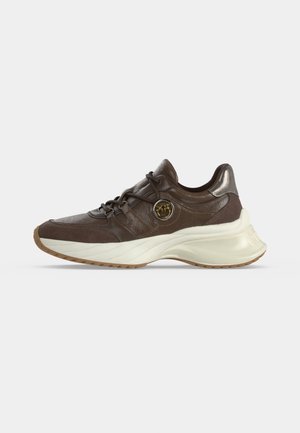 Sneaker in pelle marrone scuro con suola bianca spessa, design con lacci e ciondolo logo metallico sul lato su sfondo chiaro uniforme.