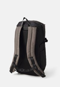 Sac à dos noir avec bretelles épaisses marron, panneau arrière en mesh, poignée de transport et boucle de poitrine réglable, vu de dos sur fond blanc.
