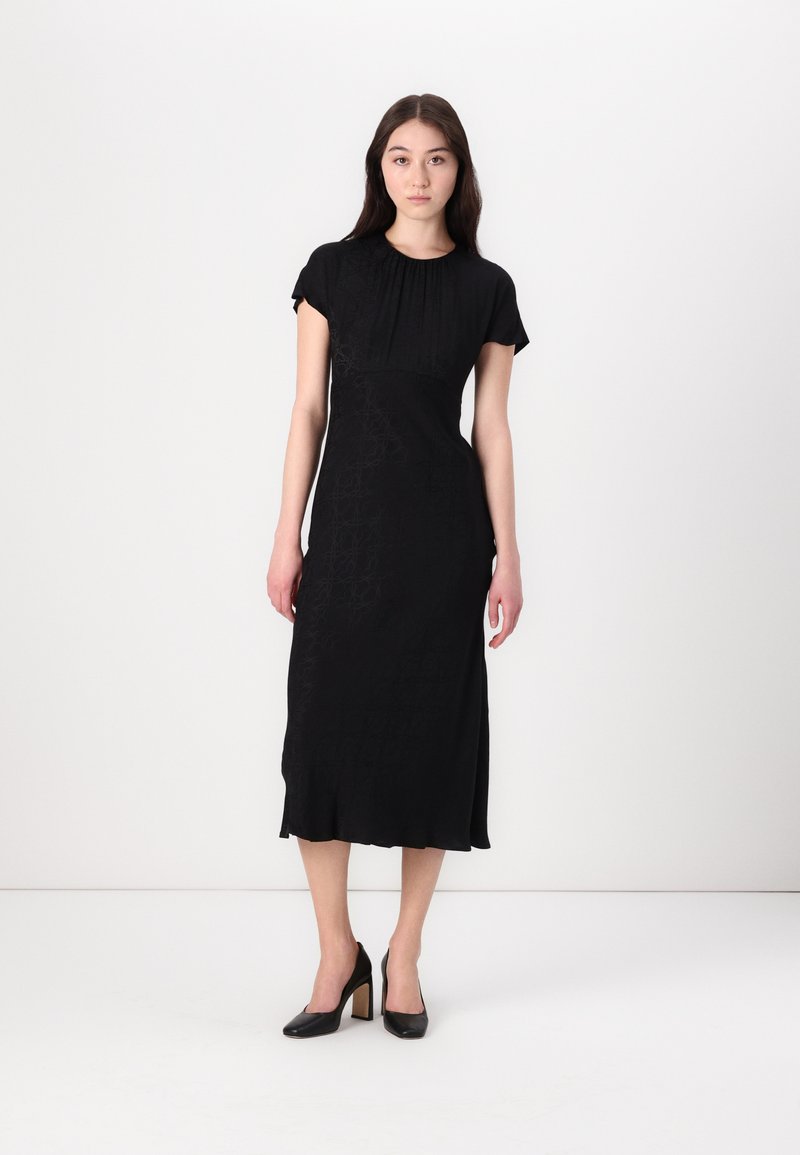 Black dress with a round neckline, short sleeves, and a fitted silhouette. Features subtle texture and a knee-length hem. Paired with block-heeled shoes.