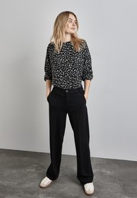 Schwarzes und weißes Leopardenmuster-Sweatshirt mit hochgerollten Ärmeln, kombiniert mit hoch taillierten schwarzen Hosen mit seitlichen Taschen und einem Druckknopfverschluss.