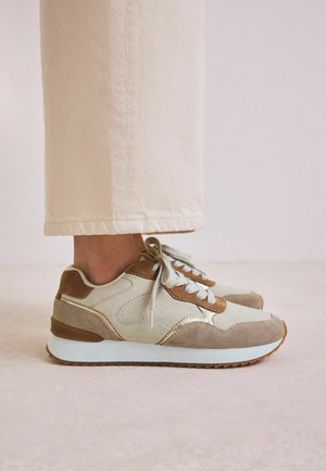Sneaker beige e marrone con texture in suede e pelle, punta arrotondata e suola bianca; presenta lacci grigi e dettagli di cucitura.