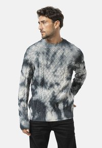 Grauer Pullover mit einem Rautenmuster aus Zopfmuster, mit Rundhalsausschnitt und gerippten Bündchen. Der Farbverlauf erzeugt einen subtilen Batikeffekt.