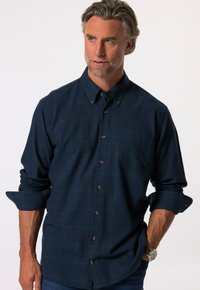 Camisa de botones azul oscuro con patrón a cuadros verdes, mangas largas remangadas, un bolsillo en el pecho y botones marrones. Textura de tela suave.