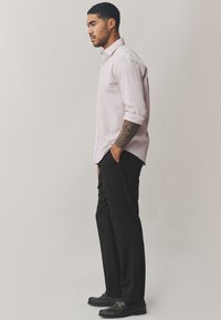 Camicia a maniche lunghe rosa chiaro con motivo strutturato, abbinata a pantaloni sartoriali neri e mocassini neri con dettagli dorati.