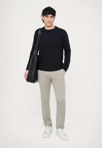 Námornícky modrý pletený sveter, svetlo béžové úzke nohavice, biele tenisky a čierna taška na rameno. Jednoduchý dizajn so štruktúrovaným vzorom na svetri.