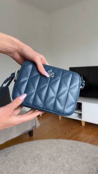 Mains tenant un sac bandoulière en cuir bleu marine matelassé avec des ferrures argentées dans un cadre de salon.