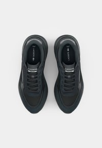 Scarpe sportive nere con tomaia in mesh e camoscio, dotate di un collare imbottito, lacci piatti e suola in gomma. Logo visibile sulla linguetta.