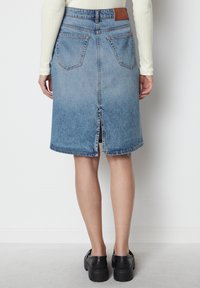 Jupe crayon en denim bleu clair avec une fente centrale à l'arrière, deux poches arrière et une étiquette en cuir marron sur la taille.