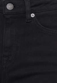 Jeans de mezclilla negra con un diseño clásico de cinco bolsillos, herrajes plateados y una textura suave con sutiles detalles de costura.