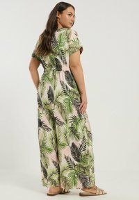 Blommig maxiklänning med en rosa bakgrund och gröna palmbladsmönster. Avslappnad passform, korta ärmar och lös, flödande silhuett.