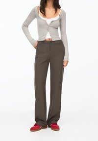 Gray long-sleeve cardigan over a white tank top paired with tailored olive green trousers and red sneakers with a gum sole.