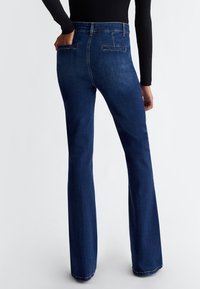 Jeans in denim blu scuro a gamba svasata con vita medio-alta, tasche posteriori e dettagli di cucitura discreti. Texture liscia con un design classico.