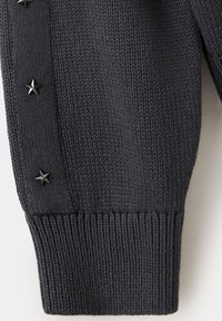 Manche de pull en tricot gris foncé avec poignet côtelé et trois boutons métalliques en forme d'étoile le long de la couture latérale.