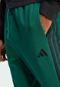Groene sweatpants gemaakt van zachte stof, met een zwart logo en zijsstrips. Elastische tailleband met een trekkoord voor aanpassing.